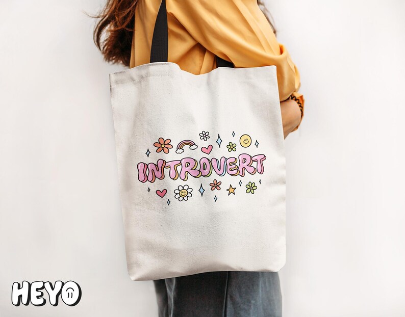 May include: White tote bag with black handles and the text "Introvert" in pink and rainbow letters with colorful flowers and stars around it.
