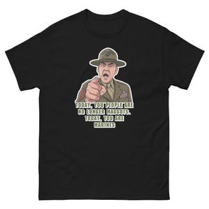 Può includere: Una t-shirt nera con un'illustrazione grafica di un istruttore in uniforme color marrone chiaro e cappello da campagna, che punta in avanti. Sotto la figura, il testo recita: TODAY, YOU PEOPLE ARE NO LONGER MAGGOTS. TODAY, YOU ARE MARINES.