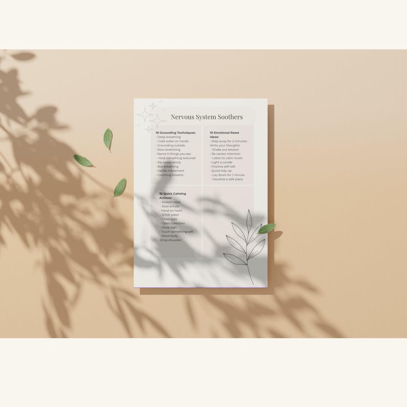 May include: A white paper titled "Nervous System Soothers" with a list of grounding techniques, emotional reset ideas, and quick calming actions. The paper is on a beige surface with shadows and green leaves.