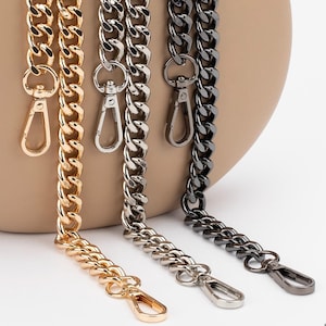 May include: Three chain straps in gold, silver, and black metal. The chains are linked together and have a lobster clasp at the end.