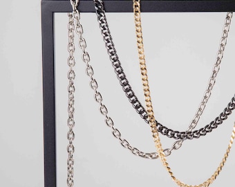 Peut inclure: Quatre colliers à chaîne différents suspendus à un présentoir noir. Les chaînes sont argentées, dorées et noires.