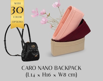 Puede incluir: Una mochila Caro Nano negra que mide 14 x 16 x 8 cm, acompañada de tres organizadores de fieltro para bolsos en rosa claro, rojo oscuro y beige. Una pancarta amarilla muestra el texto WITH 30 COLOR OPTIONS y hay flores rosas detrás.