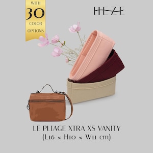 Könnte beinhalten: Eine braune Kosmetiktasche mit Tragegriff und Schulterriemen, dazu drei Filz-Taschenorganizer in Hellrosa, Dunkelrot und Beige. Der Text umfasst HEZE, WITH 30 COLOR OPTIONS und LE PLIAGE XTRA XS VANITY (L16 x H10 x W11 cm).