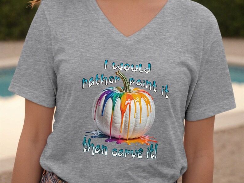 K&ouml;nnte beinhalten: Graues V-Ausschnitt-T-Shirt mit einem wei&szlig;en K&uuml;rbis, der mit Regenbogenfarben bemalt ist. Die Farbe tropft herunter. Der Text "I would rather paint it than carve it!" steht in Blau und Wei&szlig; geschrieben.