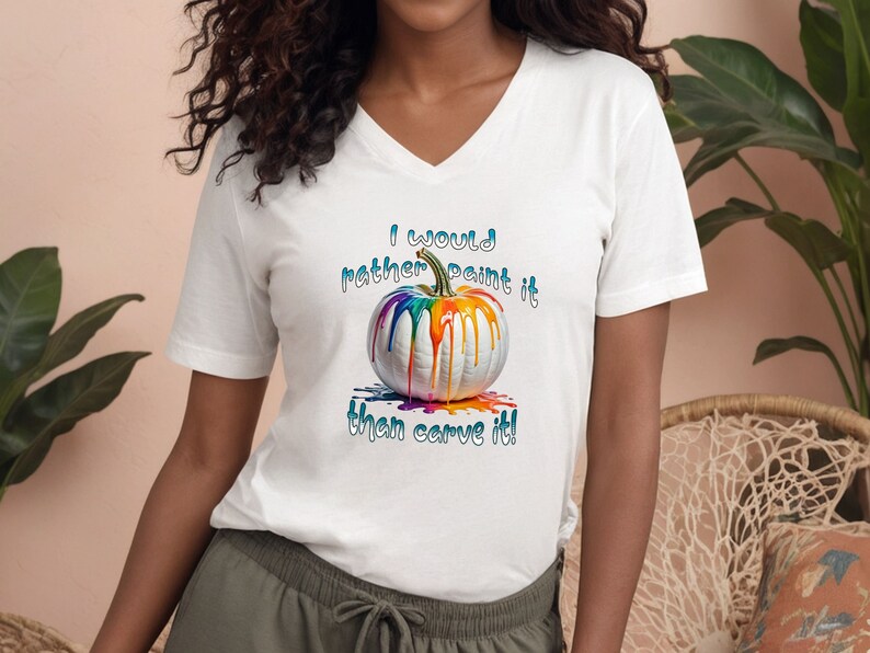 K&ouml;nnte beinhalten: Wei&szlig;es V-Ausschnitt-T-Shirt mit einem bunten, bemalten K&uuml;rbis-Design. Der K&uuml;rbis hat tropfende Regenbogenfarben. Der Text auf dem Shirt lautet: "I would rather paint it than carve it!"
