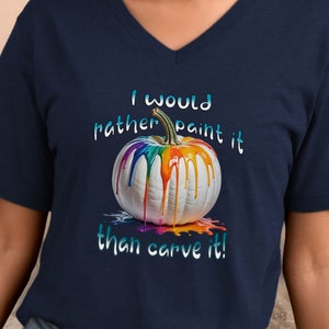 K&ouml;nnte beinhalten: Marineblaues V-Ausschnitt-T-Shirt mit einem wei&szlig;en K&uuml;rbis mit bunten Farbtropfen. Der Text "I would rather paint it than carve it!" ist oberhalb und unterhalb des K&uuml;rbisses in einer Farbverlaufs-Schrift gedruckt.