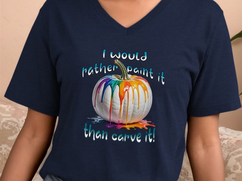 K&ouml;nnte beinhalten: Marineblaues V-Ausschnitt-T-Shirt mit einem wei&szlig;en K&uuml;rbis mit bunten Farbtropfen. Der Text "I would rather paint it than carve it!" ist oberhalb und unterhalb des K&uuml;rbisses in einer Farbverlaufs-Schrift gedruckt.