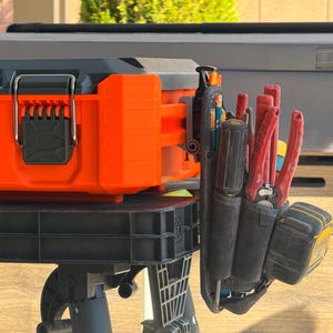 May include: An orange and black tool case with a black handle and latch. A black tool belt with various red and black tools is attached to the side. The tools include pliers, screwdrivers, and a measuring tape.