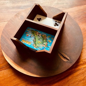 May include: A wooden card holder with two compartments. The top compartment has a playing card with the four of clubs. The bottom compartment has a map of Oahu, Hawaii. The card holder is sitting on a wooden surface.
