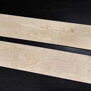 Könnte beinhalten: Zwei rechteckige Holzbretter, beide hellbraun, mit natürlicher Holzmaserung. Die Bretter liegen flach auf einer schwarzen Oberfläche.