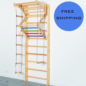 Puede incluir: Conjunto de gimnasio de pared de madera con una escalera de cuerda, una pared de escalada, anillos y un columpio. El conjunto está hecho de madera natural y tiene un acabado marrón claro. El conjunto está montado en una pared blanca. El texto "ENVÍO GRATIS" está escrito en negro sobre un círculo azul.