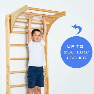 K&ouml;nnte beinhalten: Wandmontierte Klimmzugstange aus Holz mit einem Kind, das daran h&auml;ngt. Die Stange ist aus Naturholz gefertigt und hat eine abgerundete Oberseite. Das Kind tr&auml;gt ein wei&szlig;es Shirt und eine blaue Shorts. Der Text "UP TO 286 LBS/ 130 KG" ist in einem blauen Kreis sichtbar.