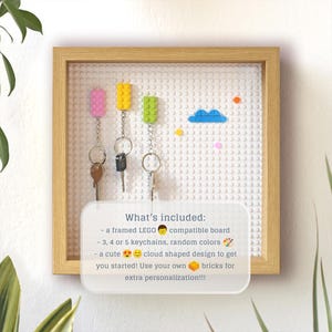 May include: A framed white LEGO compatible board with a cloud design and colourful keychains. The text "What's included:" is written on a white rectangle with a smiley face, paintbrush, and brick icons.