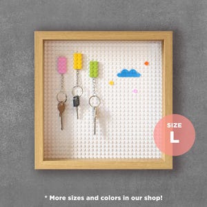 May include: A white Lego-style key holder with a wooden frame. The key holder has three keys attached to it with colourful Lego bricks. The key holder is labelled "SIZE L".