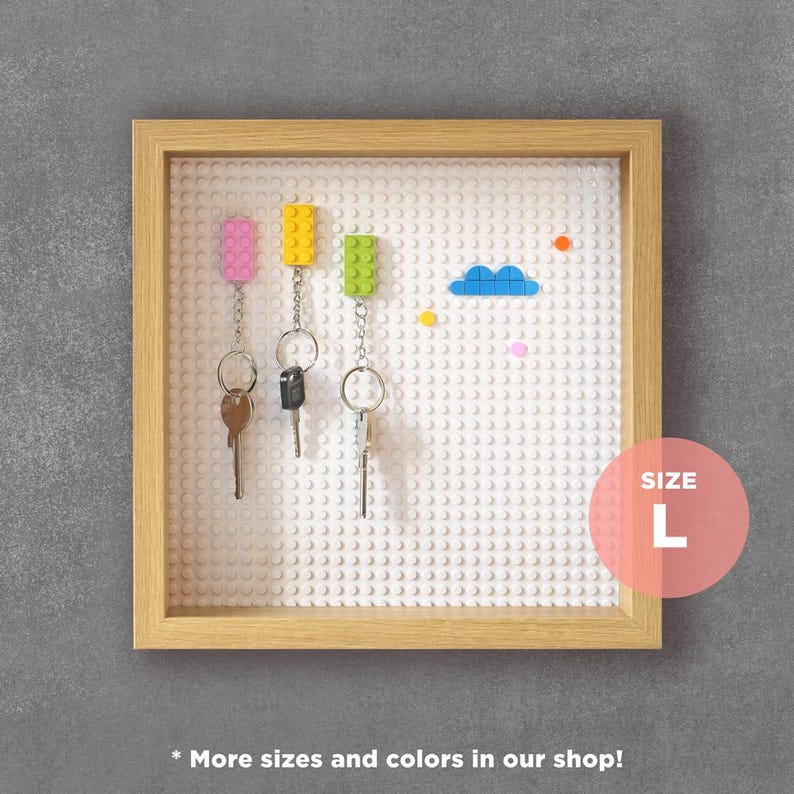 May include: A white Lego-style key holder with a wooden frame. The key holder has three keys attached to it with colourful Lego bricks. The key holder is labelled "SIZE L".