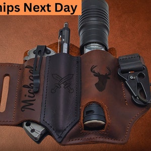 May include: A brown leather belt with a black leather pouch for carrying a flashlight, knife, and pen. The pouch has a deer silhouette and the text "Michael" engraved on it.