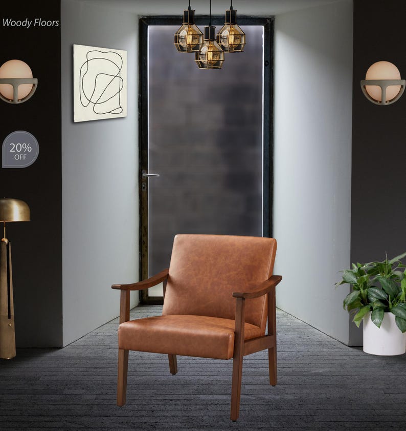 May include: A brown leather armchair with wooden armrests and legs. The chair is positioned in a room with a dark gray door and a modern light fixture. The wall art features a black abstract design.