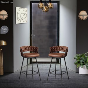 May include: Two brown leather bar stools with black metal frames and a quilted design on the backrests. The stools are set against a white wall with a door in the background. The text "20% OFF" is visible in the image.
