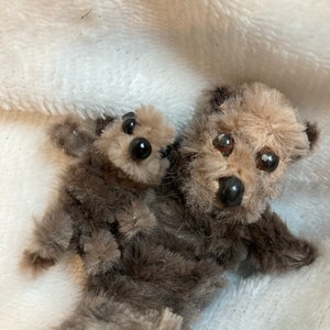 May include: Two brown plush teddy bears, one larger than the other, are sitting together. The larger bear has a brown nose and black eyes. The smaller bear has black eyes and a brown nose. Both bears have a fluffy texture.