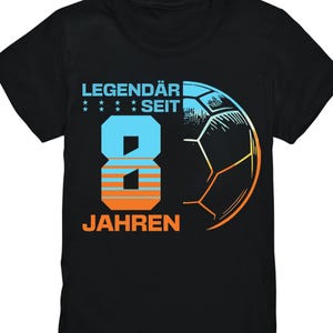 Op de afbeelding: Zwart T-shirt met een voetbalthema. Het nummer 8 is in blauw en oranje, met de woorden "LEGENDÄR SEIT" erboven en "JAHREN" eronder. Een voetbalafbeelding staat aan de rechterkant.