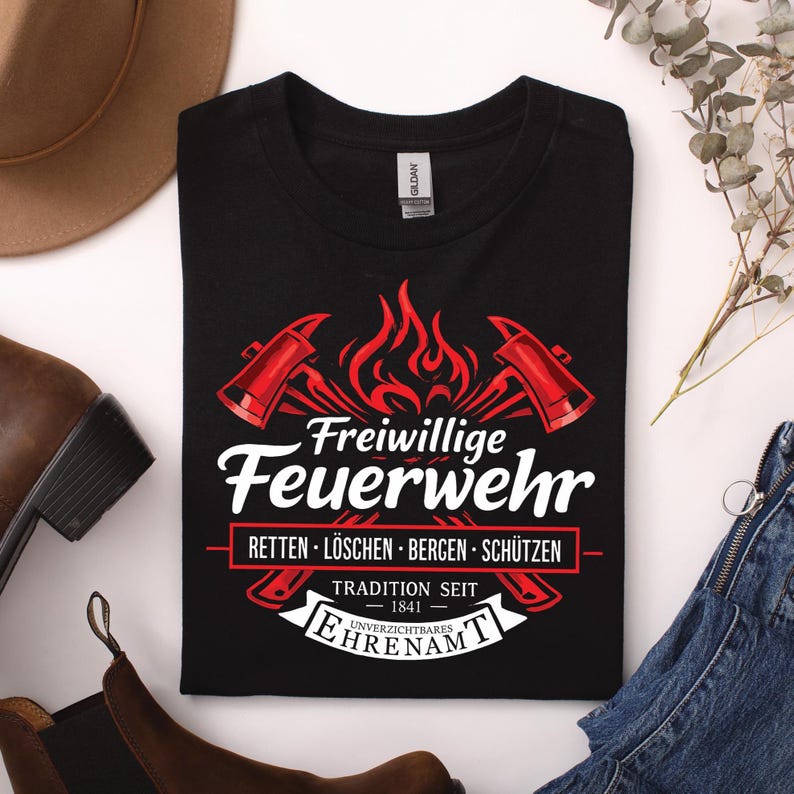 May include: Black t-shirt featuring a firefighter design. The design includes crossed axes, flames, and the words "Freiwillige Feuerwehr" in white script. Below, it reads "Rettung, L&ouml;schen, Bergen, Sch&uuml;tzen" and "Tradition Seit 1841".