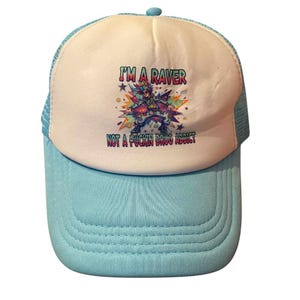 May include: A light blue and white trucker hat with the text "I'M A RAVER NOT A FUCKIN DRUG ADDICT" and a colourful graphic of a person. The hat has a curved brim and a mesh back.