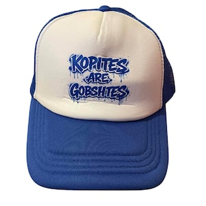 Könnte beinhalten: Blau-weiße Trucker-Cap mit dem Text "Kopites Are Gobshites" in blauer Graffiti-Schrift. Die Kappe hat einen blauen Schirm und eine weiße Frontplatte mit blauem Mesh-Rücken.