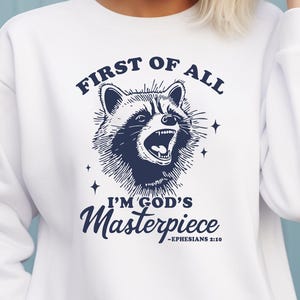 May include: White sweatshirt with a blue graphic of a raccoon with the text "First of all I'm God's Masterpiece - Ephesians 2:10"