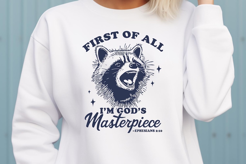 May include: White sweatshirt with a blue graphic of a raccoon with the text "First of all I'm God's Masterpiece - Ephesians 2:10"