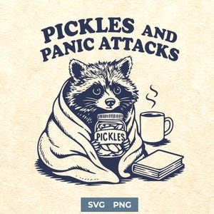 Könnte beinhalten: Eine marineblaue und weiße Illustration zeigt einen Waschbären in einer Decke, der ein Glas Essiggurken hält. Der Text "PICKLES AND PANIC ATTACKS" steht darüber. Eine Tasse und ein Buch sind ebenfalls abgebildet.