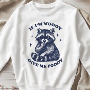 May include: White sweatshirt with a blue graphic of a raccoon with the text "If I'm moody give me foody".