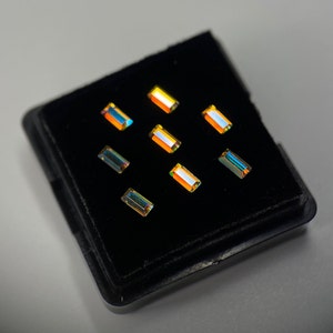 May include: A black velvet box containing nine iridescent rectangular gemstones. The gemstones are arranged in a grid pattern and have a rainbow-like sheen.