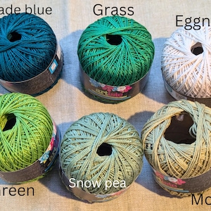 May include: Six balls of yarn in various shades of green, blue, and white. The yarn is labeled with the colors "Jade blue", "Grass", "Eggnog", "Green", "Snow pea", and "Moss".