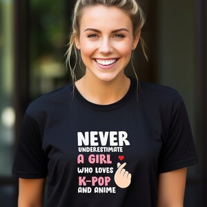 May include: Black t-shirt with white text that reads "Never underestimate a girl who loves K-Pop and anime". The text is accompanied by a pink heart and a pink hand gesture.