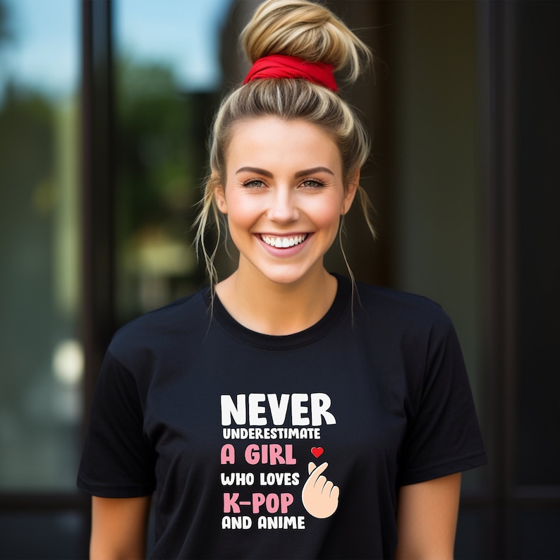 May include: Black t-shirt with white text that reads "Never underestimate a girl who loves K-Pop and anime". The text is accompanied by a pink heart and a pink hand gesture.