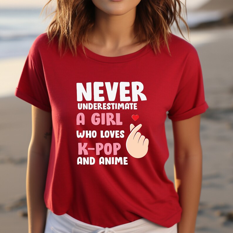 May include: Red t-shirt with the text "Never underestimate a girl who loves K-pop and anime" in white. A pink heart and a pink hand gesture are included in the design.
