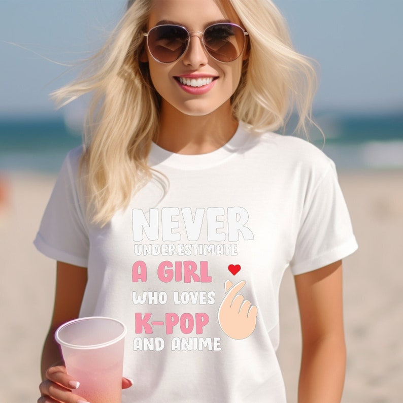 May include: White t-shirt with the text "Never underestimate a girl who loves K-pop and anime" in black and pink lettering. A pink heart and a pink hand gesture are also included in the design.