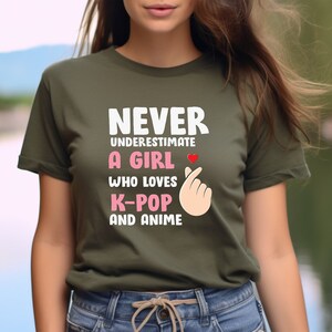 May include: Green t-shirt with the text "NEVER UNDERESTIMATE A GIRL WHO LOVES K-POP AND ANIME" and a pink heart and a pink hand gesture.