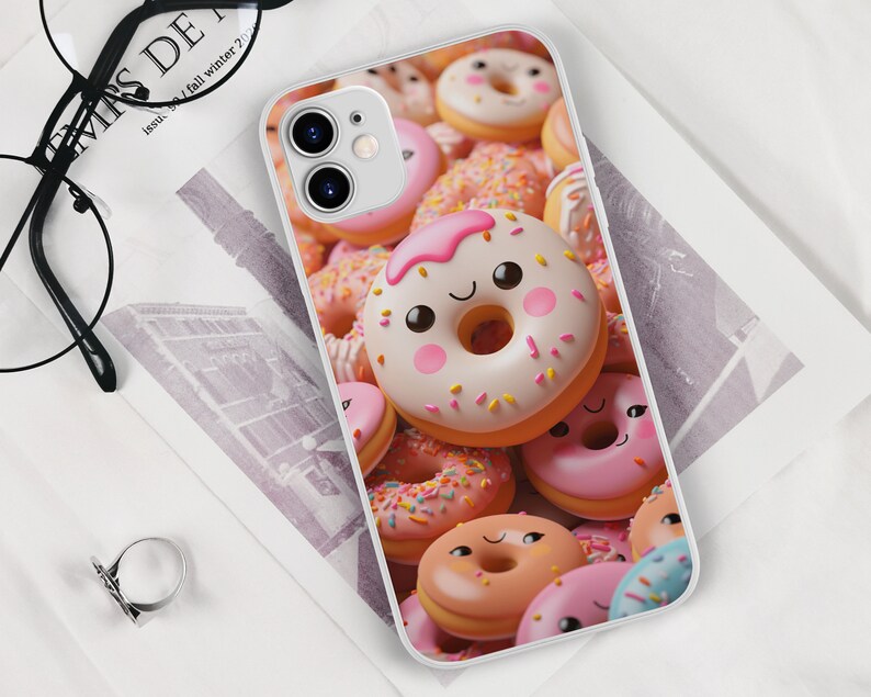May include: A white phone case with a colorful donut design. The donuts are pink, white, and brown with sprinkles and frosting. Some of the donuts have happy faces.