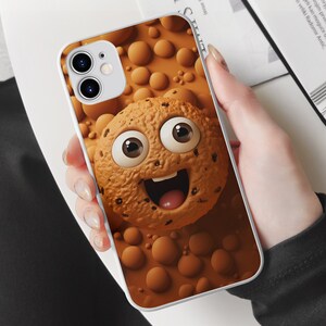 May include: White iPhone case with a brown cookie design. The cookie has a smiling face with big eyes and chocolate chips.