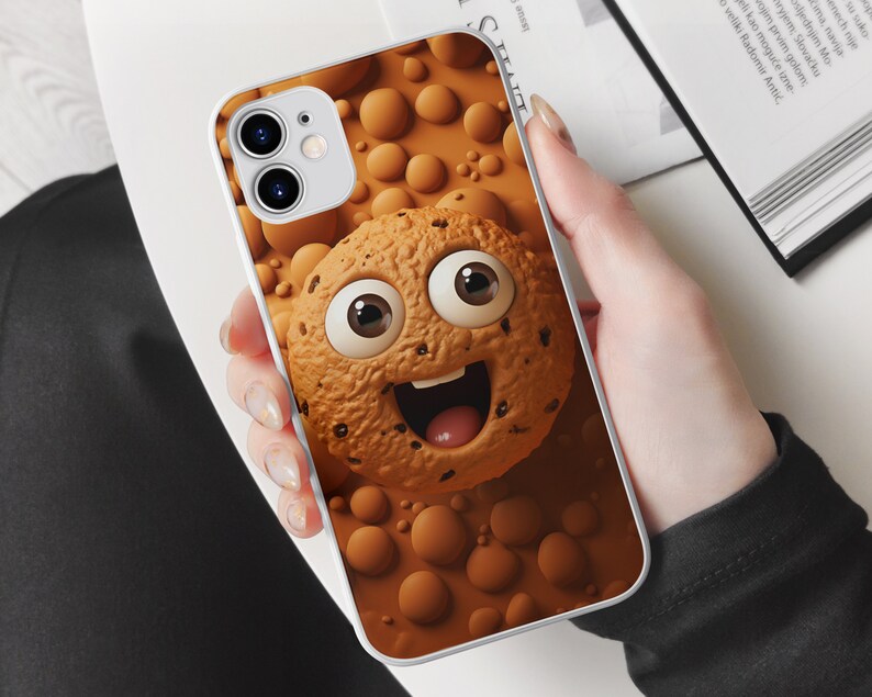 May include: White iPhone case with a brown cookie design. The cookie has a smiling face with big eyes and chocolate chips.