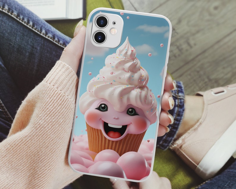 May include: A pink and white cupcake with a smiling face and sprinkles on top. The cupcake is on a white phone case with a blue sky background.