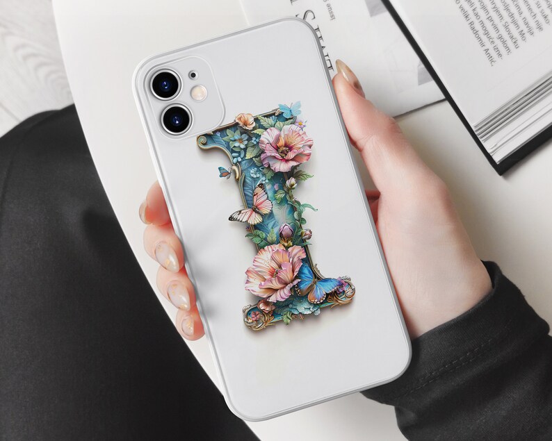 May include: A white iPhone case with a 3D floral design featuring a large letter "I" with butterflies and pink flowers. The case has a camera cutout and a white background.