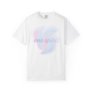 Puede incluir: Una camiseta blanca de manga corta con un gráfico central que presenta un suave remolino difuminado de colores pastel rosa, azul y morado. El texto 'one spirit' está impreso en una fuente cursiva de color morado oscuro en el centro.