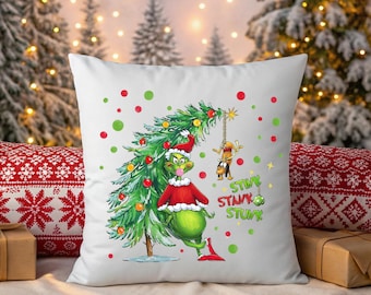 Peut inclure: Coussin carré blanc avec un personnage vert du Grinch portant un bonnet de Père Noël et un pull rouge, à côté d'un sapin de Noël. L'arbre est décoré de boules rouges et jaunes. Les mots "STINK, STANK, STUNK" sont écrits en vert.