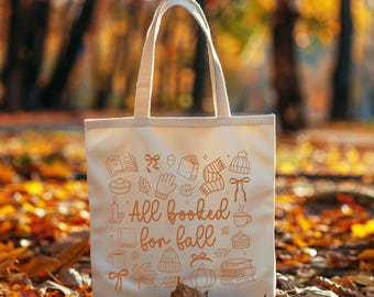 May include: Cream tote bag featuring the text "All booked for fall" and autumn-themed illustrations in orange. The design includes books, a pumpkin, a hat, and a cup of coffee. The bag has a rectangular shape and two handles.