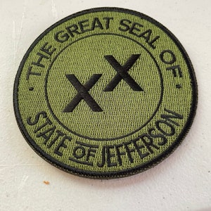 May include: Green embroidered patch with black stitching. The patch features the text "The Great Seal of the State of Jefferson" in a circle around two black "X"s.