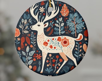 May include: Circular ceramic Christmas decoration. It features a white deer with floral patterns and large antlers, set against a dark blue backdrop with red, blue, and white floral and foliage designs. A gold string is attached for hanging.