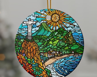 May include: Circular ceramic Christmas decoration with a stained-glass effect showing a coastal scene, including a mountain, sun, and Christ the Redeemer statue. The ornament has a gold hanging string and is decorated with bright colours.