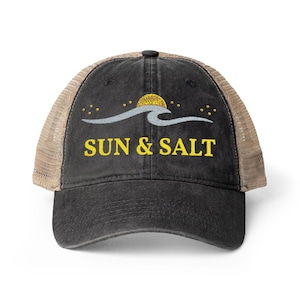 May include: A black baseball cap with a tan mesh back. The front features an embroidered design of a yellow sun, a light gray wave, and small yellow stars. Below the graphic, the text SUN & SALT is embroidered in yellow capital letters.